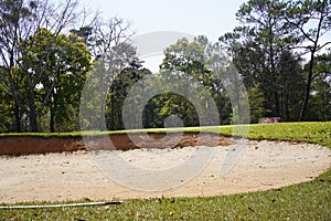 Sand bunker on the golf course with green grass and trees over blue sky