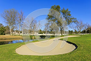 Sand bunker on the golf course with trees and pond