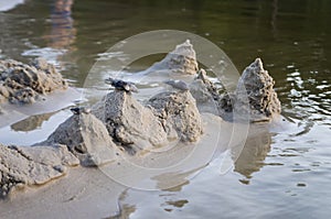 Sand castles on the bank of river. Mild background with pastel colors and reflections in the water