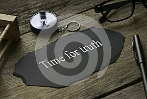 Sand clock, compass, pen, glasses and a piece of black paper written with Time For Truth on wooden background