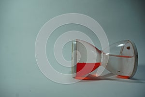 Sand clock is laying down some red liquid inside it on white background