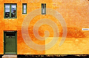 Sand colours house wall with the green door and windows