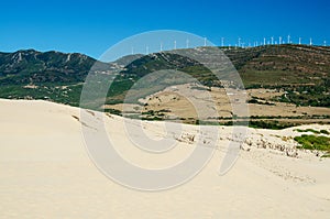 Sand dune and green mountains with windmills on the background. Punta Paloma beach. Tarifa, province of Cadiz, Spain.