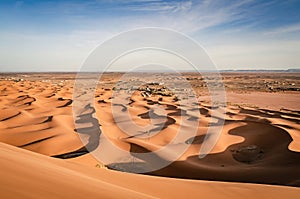 Sand dune landscape with a small village. Vast desert land of Erg Chebbi. Beautiful view towards the horizon