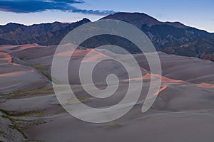 Sand dunes outlined in pink and purple sunset light in Great Sand Dunes National Park, backed by the Rocky Mountains