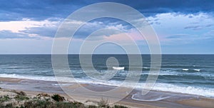 Sand dunes and waves breaking on an endless beach under a stormy sky at sunrise