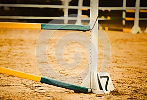 A sand field with a yellow barrier set up for horse jumping, but there is no horse in sight. The equestrian sport and discipline