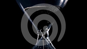 The sand flow in the hourglass with black background and lateral light backlight