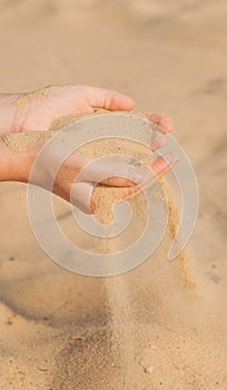 Sand flowing through the woman`s hands on the beach