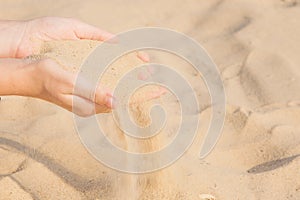 Sand flowing through the woman`s hands on the beach