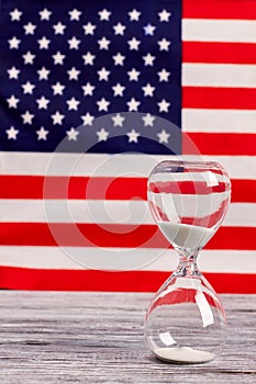 Sand glass on wood with American flag in the background.