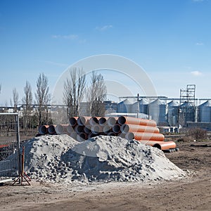 Sand, gravel and Stack of new orange polypropylene pipes in front of the railway crossing. Plastic pipes for laying in the gutter
