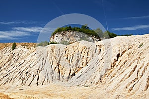 Sand hill with trees in quarry under deep blue sky