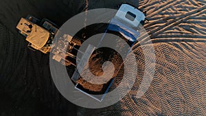 Sand mining industry, sand mine at the quarry. Scene. Aerial top view of a bulldozer machine putting sand to the truck