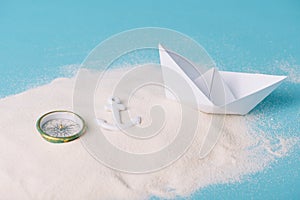 Sand with paper boat, compass and anchor