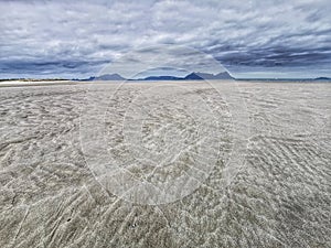 Sand patterns on sandy ocean beach under moody cloudy sky