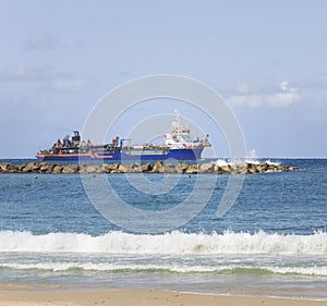 The sand pumping vessel sails along the breakwater close to the coastline