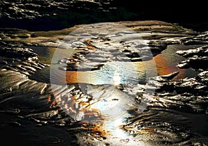 Sand and rock pool with rainbow colors from the sun reflecting in it