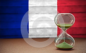 Sand running through the bulbs of an hourglass measuring the passing time in a countdown to a deadline, on France flag background