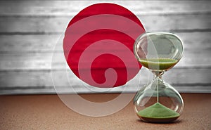 Sand running through the bulbs of an hourglass measuring the passing time in a countdown to a deadline, on Japan flag background
