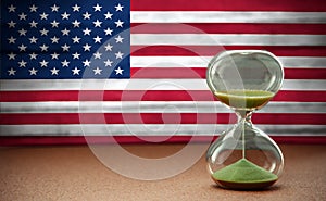 Sand running through the bulbs of an hourglass measuring the passing time in a countdown to a deadline, on USA flag background