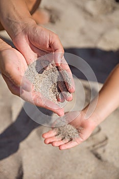 Sand running through female hands into kid`s hands.Young woman with sand in her hands playing with a child