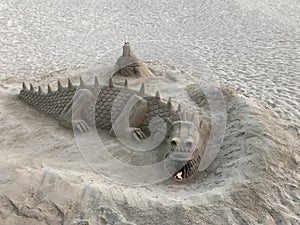 A sand sculpture in the shape of a dragon that exhales fire from the mouth located on the beach