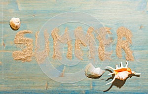 Sand and shells on blue planked wood with the word Summer. Background with copy space. Top view