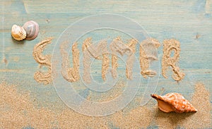 Sand and shells n blue planked wood with the word Summer. Background with copy space. Top view