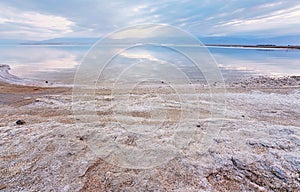Sand and stones covered with crystalline salt on shore of Dead Sea, calm clear water near - typical scenery at Ein Bokek beach,