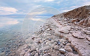 Sand and stones covered with crystalline salt on shore of Dead Sea, clear water near - typical scenery at Ein Bokek