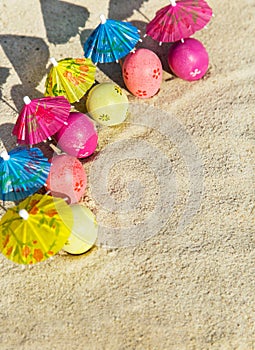 Sand texture (background) with colorful easter eggs with umbrellas on the beach.