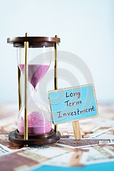 Sand timer with Long term investment sign board on currency notes - concept of future financial and retirement plans