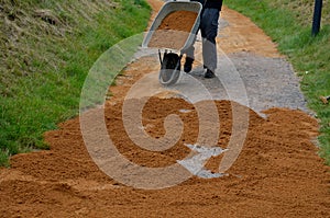 Sand wheeling. garden wheelbarrow carries a worker and pours on piles of beige gravel to repair park, forest, dirt road. erosion c