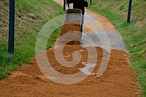 Sand wheeling. garden wheelbarrow carries a worker and pours on piles of beige gravel to repair park, forest, dirt road. erosion c