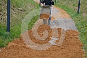 Sand wheeling. garden wheelbarrow carries a worker and pours on piles of beige gravel to repair park, forest, dirt road. erosion c