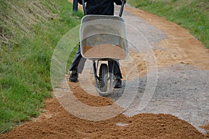 Sand wheeling. garden wheelbarrow carries a worker and pours on piles of beige gravel to repair park, forest, dirt road. erosion c