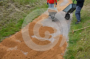 Sand wheeling. garden wheelbarrow carries a worker and pours on piles of beige gravel to repair park, forest, dirt road. erosion c