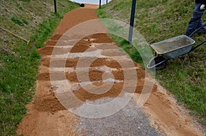 Sand wheeling. garden wheelbarrow carries a worker and pours on piles of beige gravel to repair park, forest, dirt road. erosion c