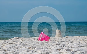 Sandcastle on white ocean beach sand. Colorful pink toy bucket lying beside seaside sandcastle.