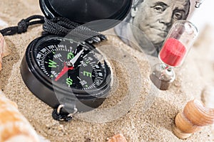 Sandglass, dollar and compass on sand isolated on white.