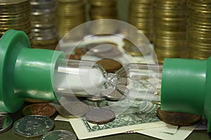 Sandglass put on coins and USA banknotes background: time is run out, it is time for making money