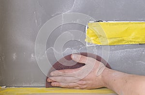 Sandpaper held in grip of man`s hand, refinishing piece of custom stucco wall