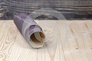 sandpaper twisted into a roll lies on a wooden board. Close-up. There is a tint