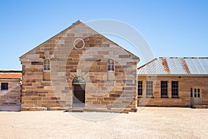 Sandstone brick convict built building with decorative stonework, corrugated iron roof, arched doorway, pebbled courtyard against