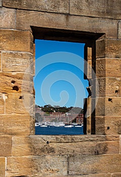 Sandstone brick wall with open window showing boats on water against blue sky