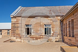 Sandstone convict brick made building with corrugated iron roof, open windows, pebbled courtyard against blue sky