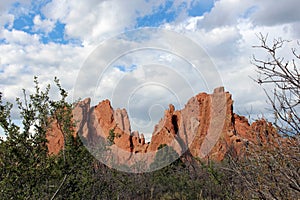 Sandstone rock formations towering above a tree line and backed by cumulus clouds at the Garden of the Gods in Colorado