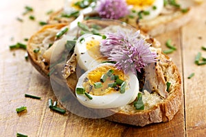 Sandwich with adition of mackerel fish , eggs and edible flowers of chives on wooden table