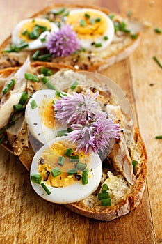 Sandwich with adition of mackerel fish , eggs and edible flowers of chives on wooden table